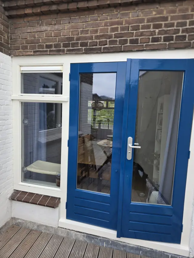 Blauw gelakte openslaande deuren met wit kozijn in een bakstenen gevel